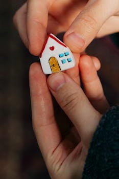 Close-up of hands holding a small handmade house figurine symbolizing home and family.