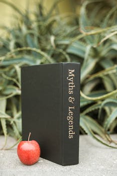 A vertical shot of a 'Myths & Legends' book next to a red apple, surrounded by green leaves.